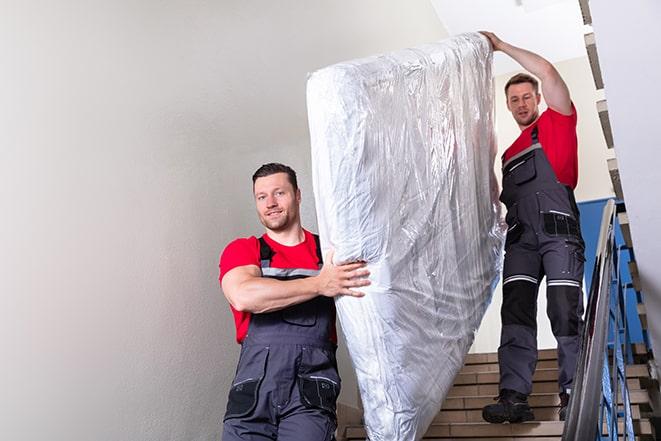 two workers safely transporting a box spring out of a house in Macomb, MI